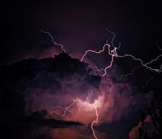 lightning strikes through the night sky with clouds in the foreground and trees to the side