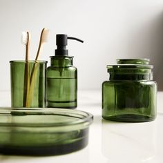 green glass containers with toothbrushes and soap dispenser