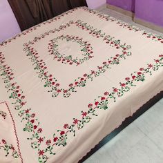 a bed covered in a white blanket with red and green flowers on the coverlet