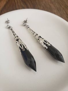 This is a pair of Resin Black Crystal Dangly Earrings. The Crystal is a Prism shape with a faceted pointy end.   Loving how many types of style and personalities this pair of earrings fit into.  You can wear it in the evening, or for an occasional event. The black and silver has a sophisticated, mysterious feel to it.  Material: * UV Resin. * Iron bead cap. * The Studs earrings are stainless steel. * Clip-on is available. Clips are brass. The earrings size is indicated in the photos. They are li Dark Angel Costume, Royal Au, Wings Earrings, Gothic Jewellery, Dark Jewelry, Oc Reference, Angel Costume, Black Gems, Earrings Aesthetic