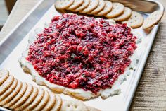 a platter with crackers and cheese covered in cranberry sauce on it