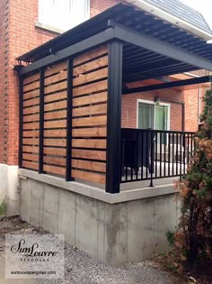 an outdoor covered patio in front of a brick building with black railings and wood slats