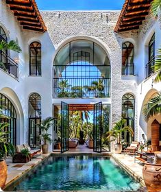 an indoor swimming pool surrounded by palm trees and potted plants in front of a large white building