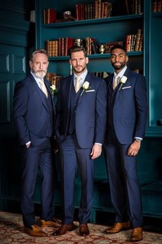 three men in suits and ties standing next to each other near bookshelves with shelves full of books behind them