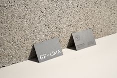 two business cards are placed next to each other on the concrete wall, which reads gf - llma