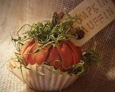 a small orange pumpkin sitting on top of a white cupcake liner covered in green sprouts