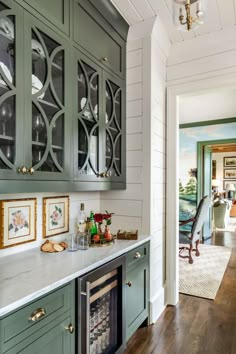 a kitchen with green cabinets and white walls, hardwood floors, and a built - in wine cooler