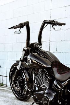 a black motorcycle parked in front of a white brick wall with the handle bars down