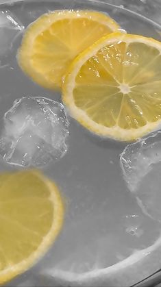 three lemons sitting on top of ice in a glass bowl with water and two slices of lemon