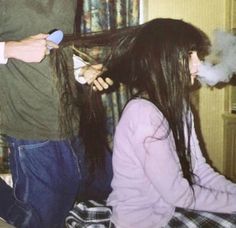 a woman blow drying her long hair with an electric razor while a man looks on