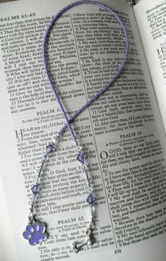 an open book with a purple beaded necklace on it and a dog paw charm