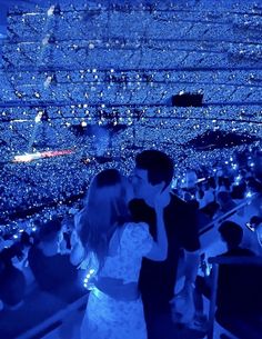 a man and woman kissing in front of an audience at a concert with blue lights