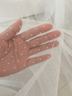 a person's hand with white dots on it sitting in front of a veil