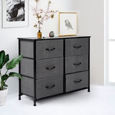 a black and grey dresser sitting next to a potted plant in a white room