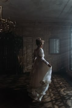 a woman in a white dress is walking through an old room with a chandelier