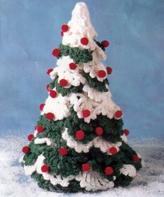 a crocheted christmas tree with red and white balls on the top, in front of a blue background