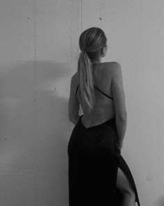 a woman in a black dress leaning against a wall with her back to the camera