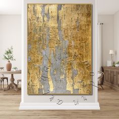 an abstract painting in gold and silver on a white wall above a wooden table with chairs