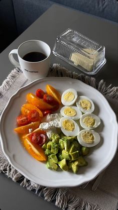 eggs, tomatoes, avocado, and other vegetables on a white plate next to a cup of coffee