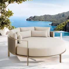 a round couch sitting on top of a white floor next to a large body of water