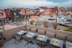 an outdoor seating area with tables and chairs on top of a roof overlooking the city