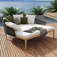 a couch with pillows on it sitting on a deck next to the water and palm trees