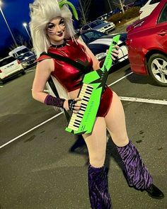 a woman dressed in costume and holding an electric keyboard on the parking lot at night