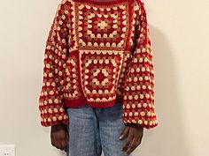 a man standing in front of a white wall wearing a red and gold knitted sweater