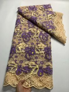 a hand is holding up a purple and gold lace