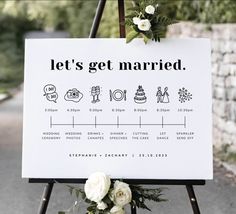 a sign that says let's get married on it with flowers and greenery