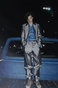 a man standing in the back of a blue pick up truck with his hands in his pockets