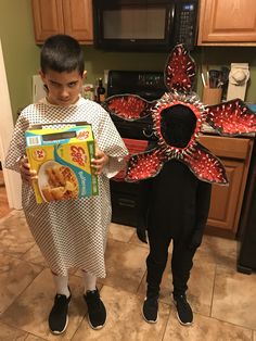 two children in costumes standing next to each other with food on their heads and holding a box