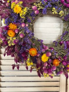 a wreath with purple, yellow and orange flowers hanging on a white shuttered wall