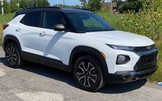 a white suv is parked on the side of the road in front of some tall grass