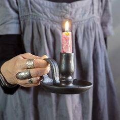 a woman is holding a candle in a metal holder with a ring on the handle