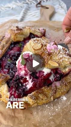 a person cutting into a berry pie on top of a piece of parchment paper with a knife