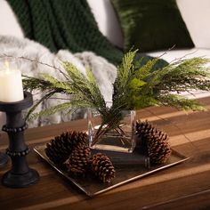 a glass vase filled with pine cones sitting on top of a table next to a candle