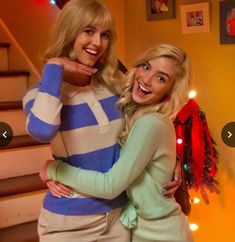 two women standing next to each other in front of stairs