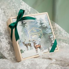 a christmas card with two deer in the snow and a green ribbon tied around it