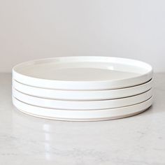 four white plates stacked on top of each other in front of a marble countertop