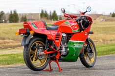 a red and green motorcycle parked on the side of a road next to a field