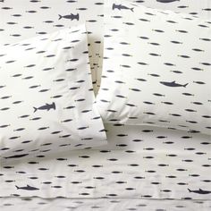 a bed with white sheets and black fish print on the sheet set, along with two pillow cases