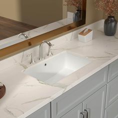 a bathroom sink sitting under a large mirror next to a counter top with two vases on it