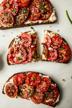 four slices of toast with tomatoes and herbs on top, sitting on a white surface