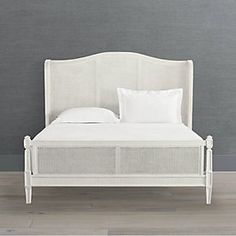 a bed with white linens and pillows against a gray wall