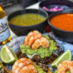 a plate topped with shrimp and guacamole next to bowls of salsa