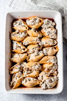 a white casserole dish filled with shells covered in cheese and meat sauces