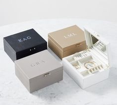 three jewelry boxes sitting on top of a white table next to each other with rings in them