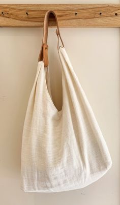 a white linen bag hanging on a wooden hanger with a leather hook in front of it