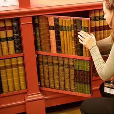 a woman sitting on the floor in front of a book shelf filled with old books